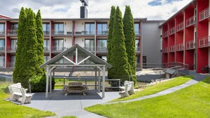 A modern building with a red facade, a covered outdoor seating area, and two tall green trees. - Hawthorn Extended Stay by Wyndham Chambersburg (Chambersburg)