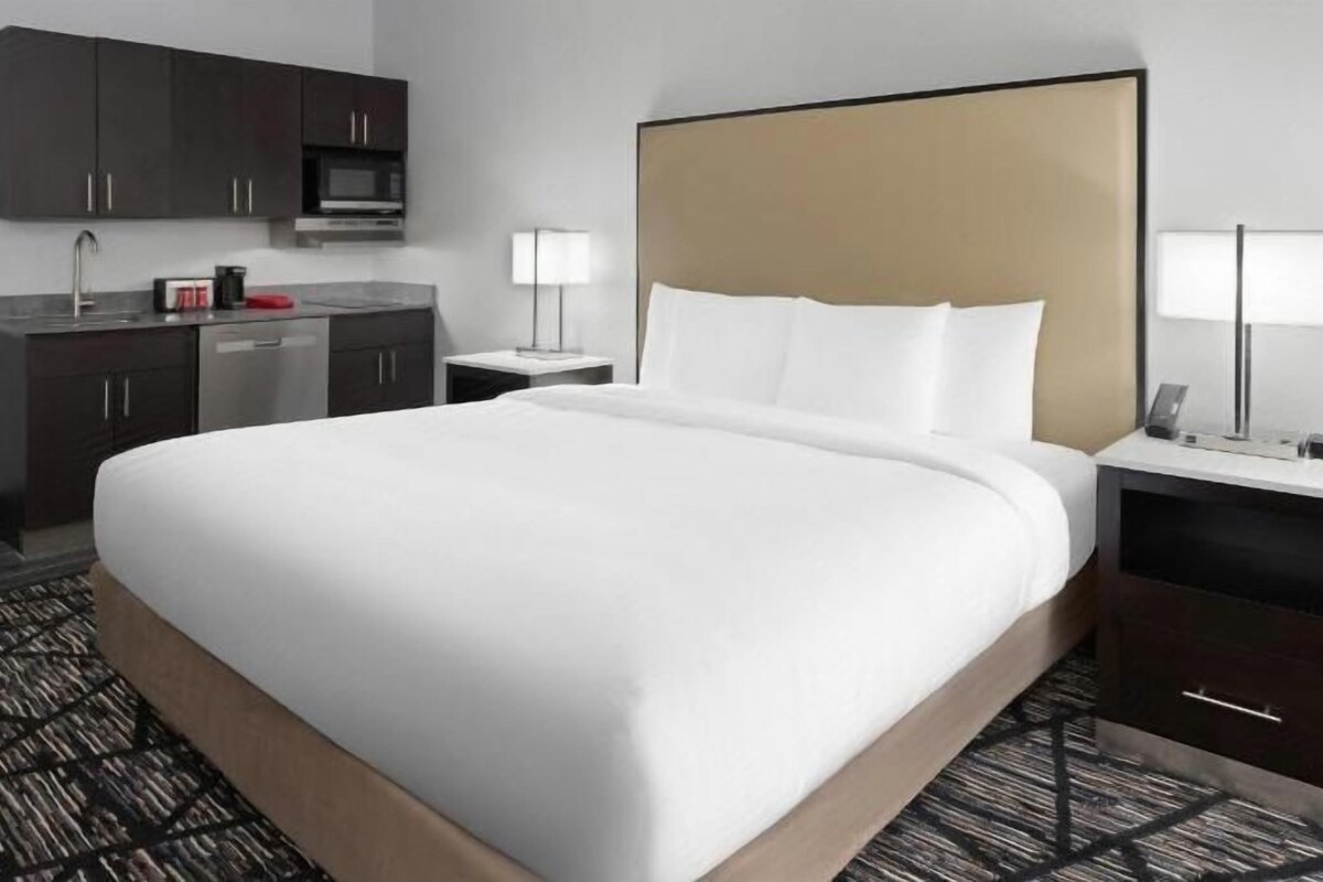A hotel room with a large bed, a desk with a lamp, a microwave, and a small kitchenette.