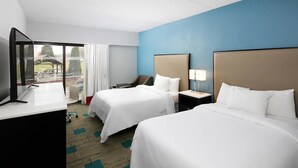 A hotel room with two beds, a desk, a TV, and a view of the outdoors.