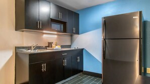 A compact kitchen with dark cabinets, a stainless steel refrigerator, and a microwave. - Hawthorn Extended Stay by Wyndham Chambersburg (Chambersburg)