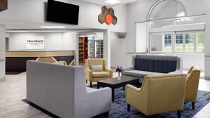 A modern hotel lobby with a grey sofa, yellow armchairs, a coffee table, and a TV mounted on the wall. - Hawthorn Extended Stay by Wyndham Chambersburg (Chambersburg)