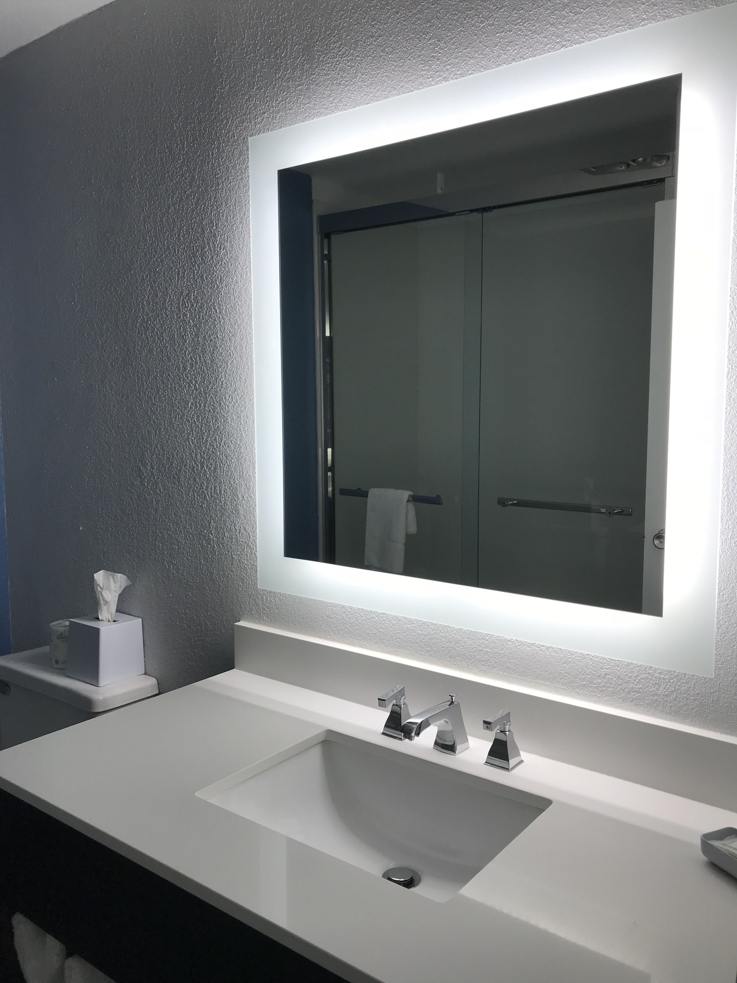 Un baño moderno con un espejo grande, dos lavamanos y un perchero para toallas.