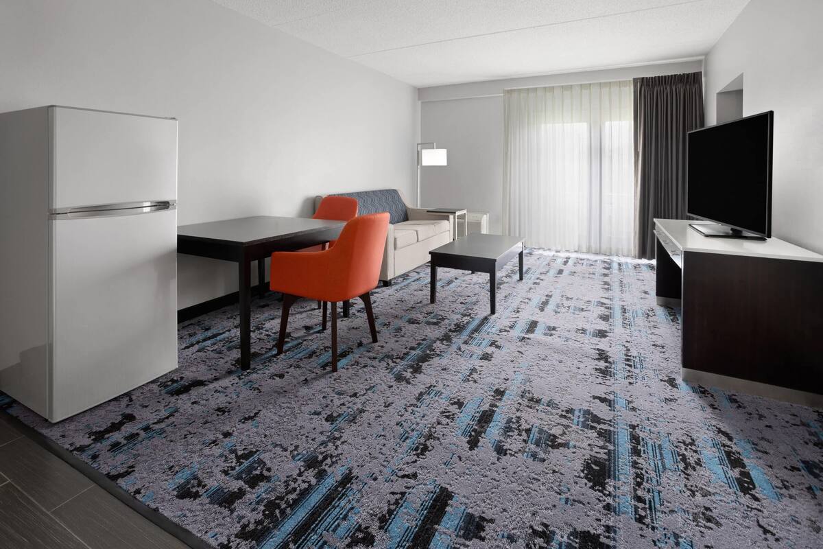 Ein Hotelzimmer mit Küchenzeile, einem Essbereich mit Tisch und Stühlen, einer Couch, einem Flachbildfernseher und einem gemusterten Teppich.