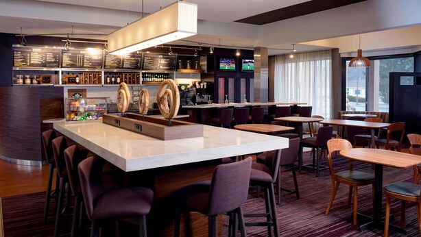 A modern bar area with a central island, bar stools, and a seating area with tables and chairs. - Sonesta Select Kansas City South Overland Park (Kansas City)