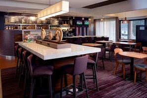Eine moderne Bar mit einer zentralen Barinsel, Barhocker und einer Sitzecke mit Tischen und Stühlen.