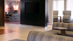A modern hotel lobby with a flat-screen TV mounted on a dark wall, a seating area with patterned sofas, and a reception desk with a decorative vase. - Sonesta Select Kansas City South Overland Park (Kansas City)