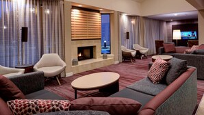 A modern hotel lobby with a fireplace, comfortable seating, a flat-screen TV, and a view of the cityscape. - Sonesta Select Kansas City South Overland Park (Kansas City)