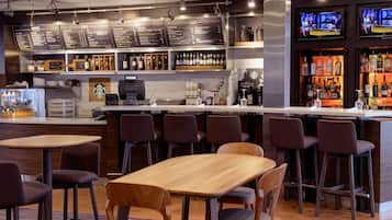 A bar area with multiple seating options, including tables and bar stools, a counter with a cash register, and shelves stocked with bottles.