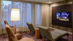 A hotel room with a TV, two armchairs, a round wooden side table, and a floor lamp. - Sonesta Select Kansas City South Overland Park (Kansas City)