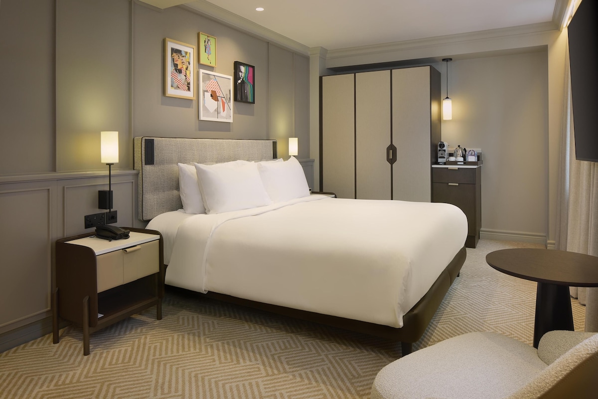 Una habitación de hotel con cama, mesita de noche, lámpara, silla y armario.