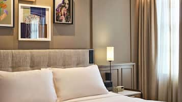 Una habitación de hotel con una cama bien hecha, una mesita de noche con lámpara y cuadros en la pared.