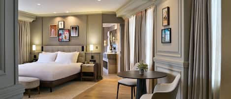 A hotel room with a large bed, a small table with chairs, a desk, and a bathroom visible through an open door.