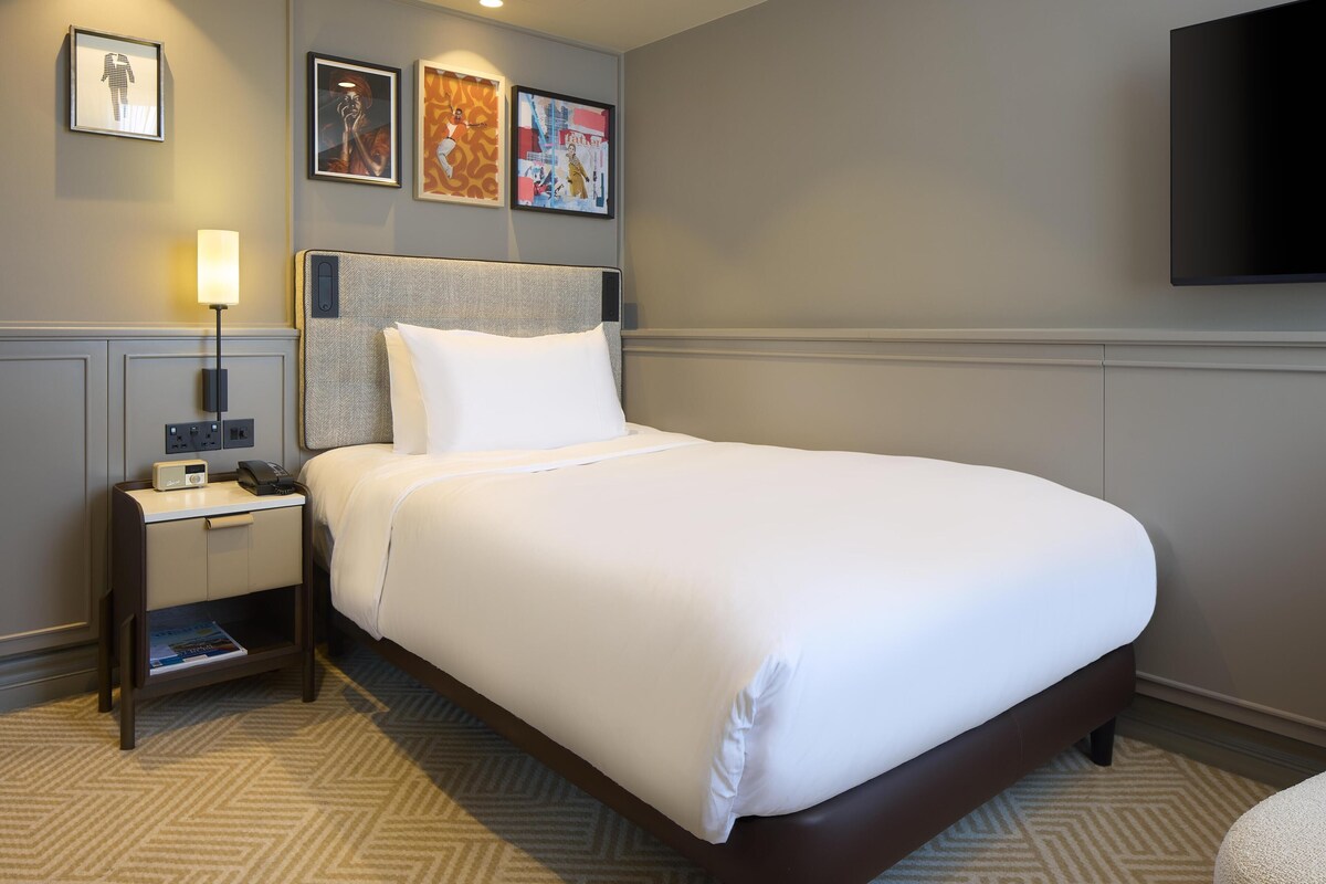 Habitación de hotel con cama, mesita de noche, lámpara y decoración en la pared.