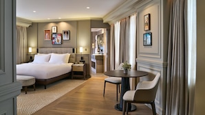 Habitación de hotel con una cama grande, una pequeña mesa con sillas, un escritorio y un baño visible a través de una puerta abierta.