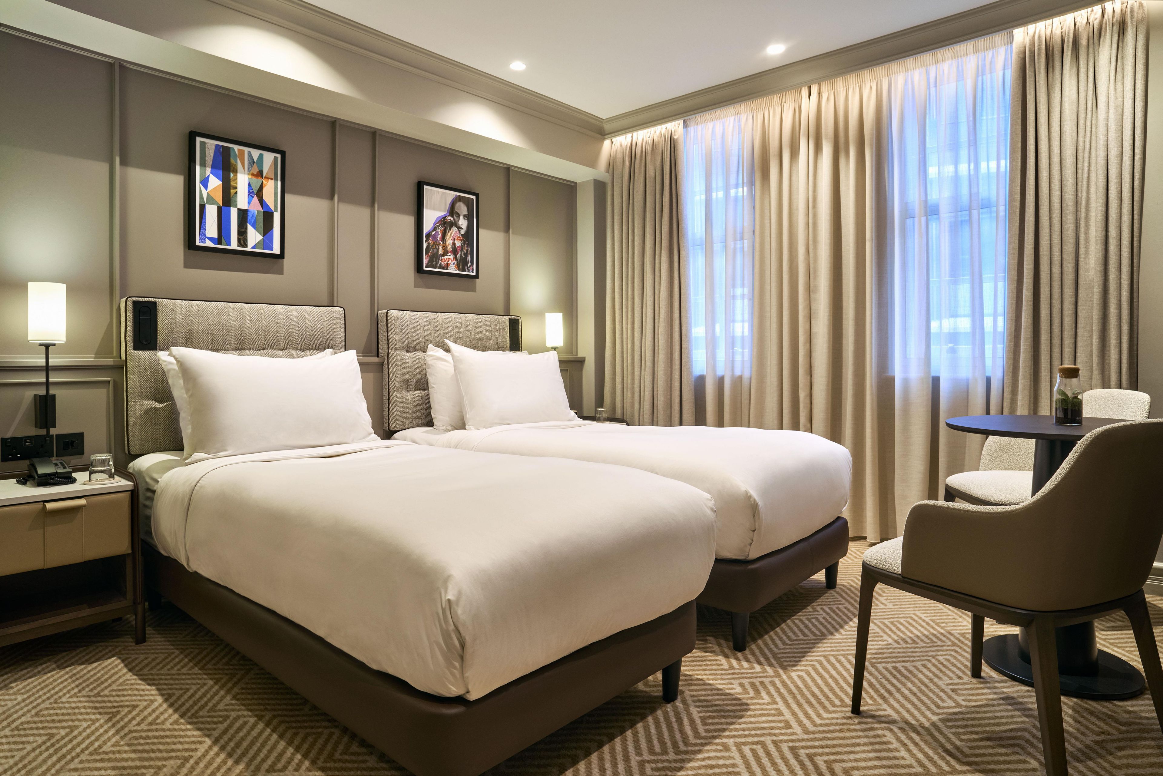 A hotel room with two beds, a desk, a chair, and a small table.
