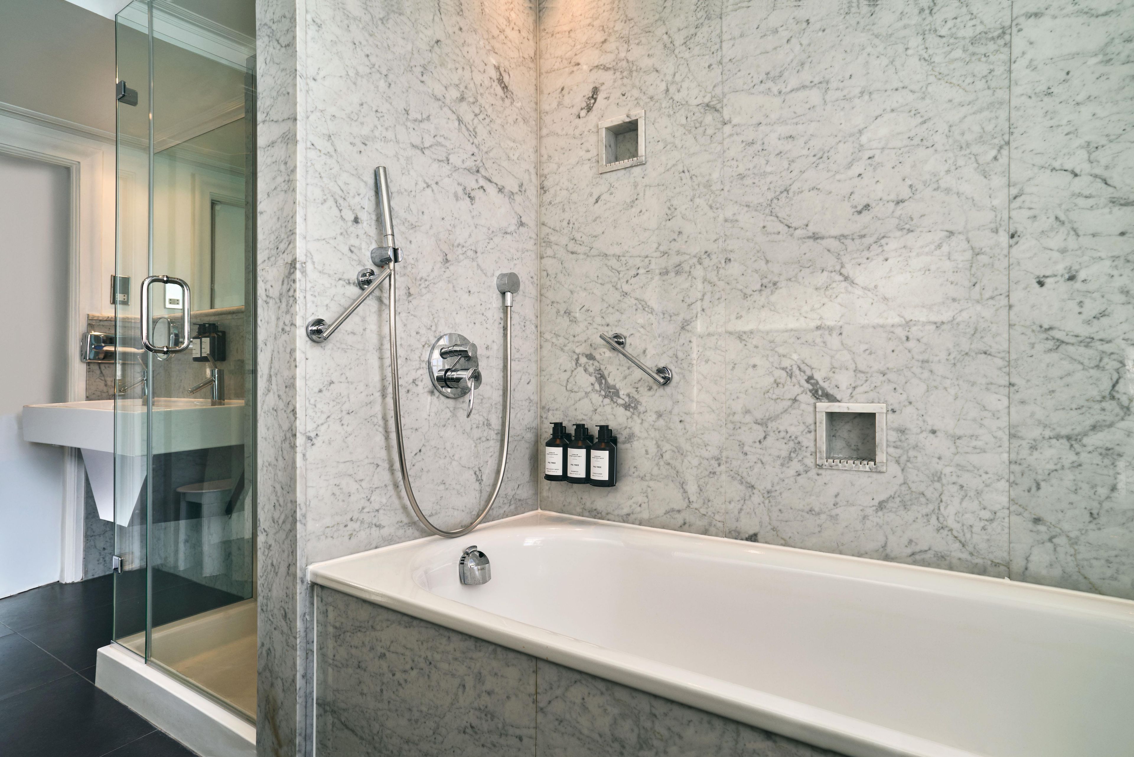 A modern bathroom with a marble wall, a glass-enclosed shower, and a white bathtub.