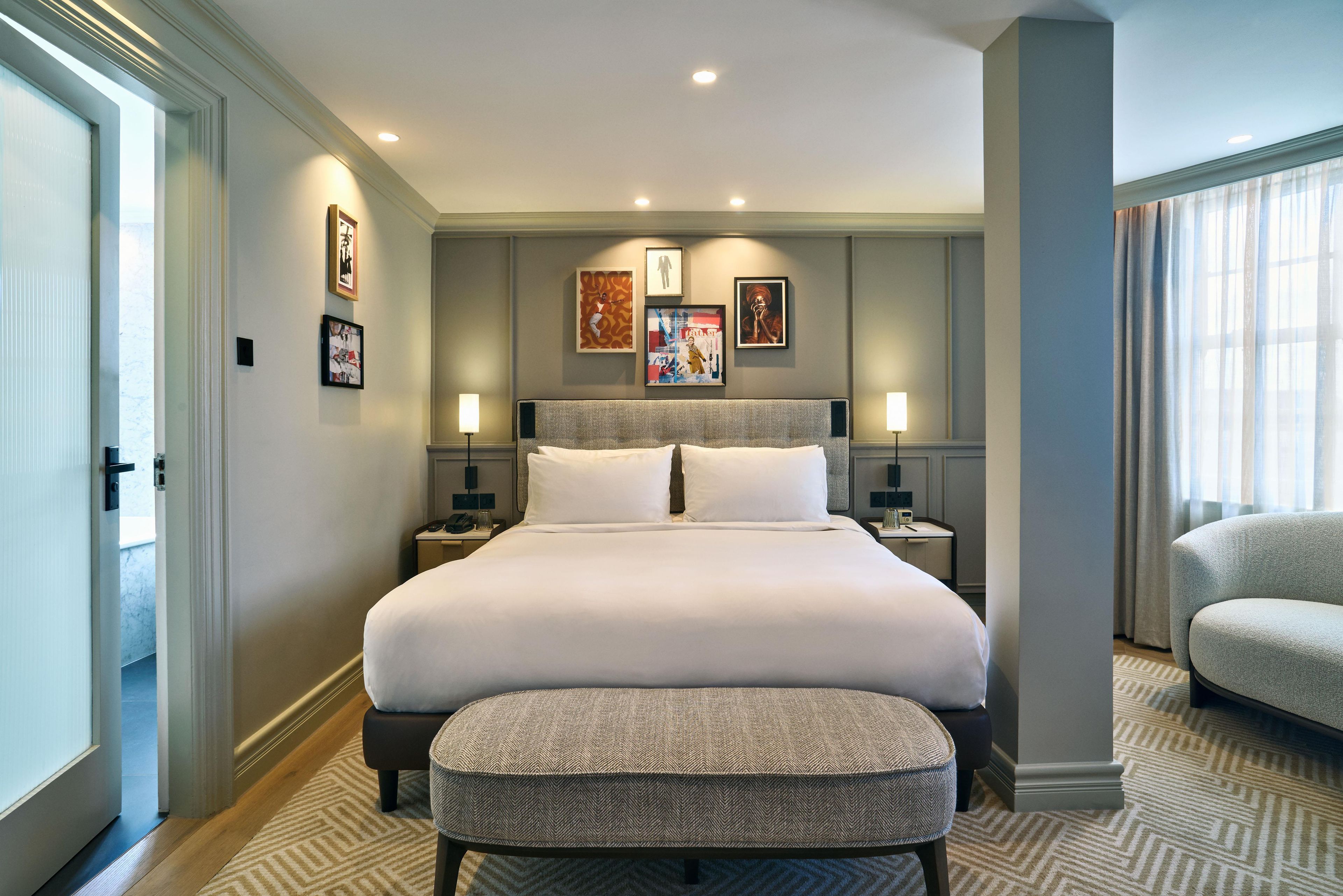 A hotel room with a large bed, a bedside table, a nightstand, a chair, and a window with curtains.