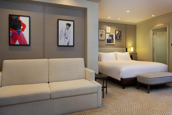 A hotel room with a sofa, a bed, a small table, and a wall with framed artwork.