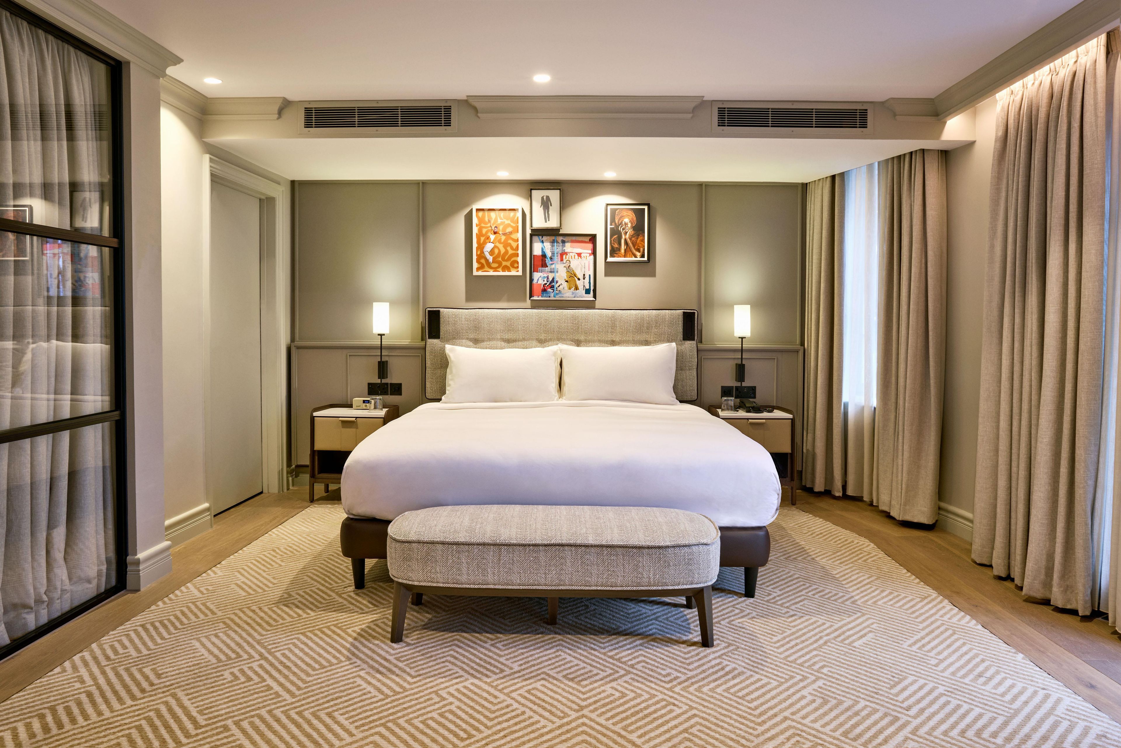 A large bed with a headboard, two bedside tables, a bench, and a patterned carpet.