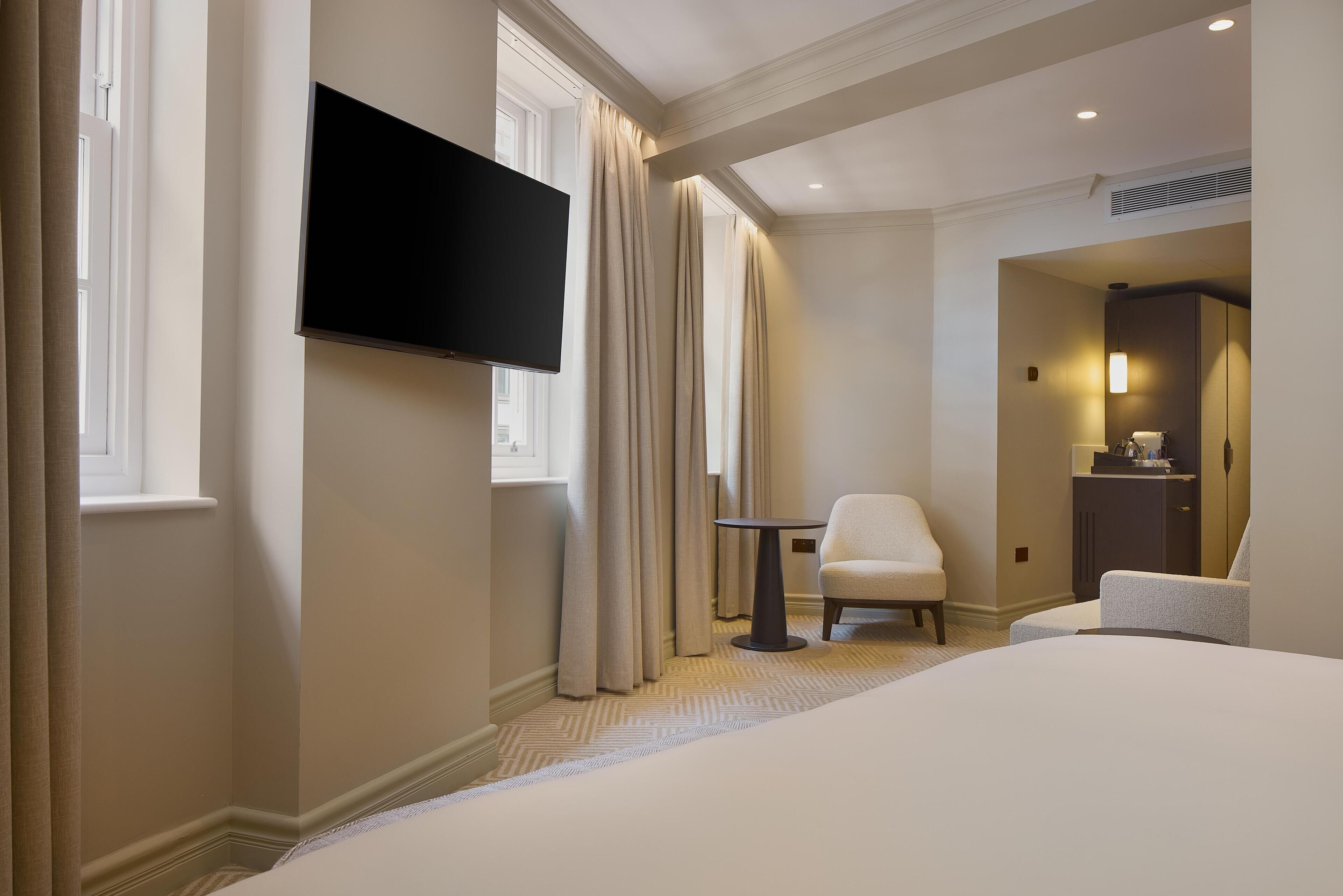 A hotel room with a bed, a TV mounted on the wall, a chair, and a small table.