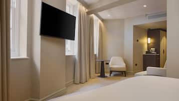 A hotel room with a bed, a TV mounted on the wall, a chair, and a small table.