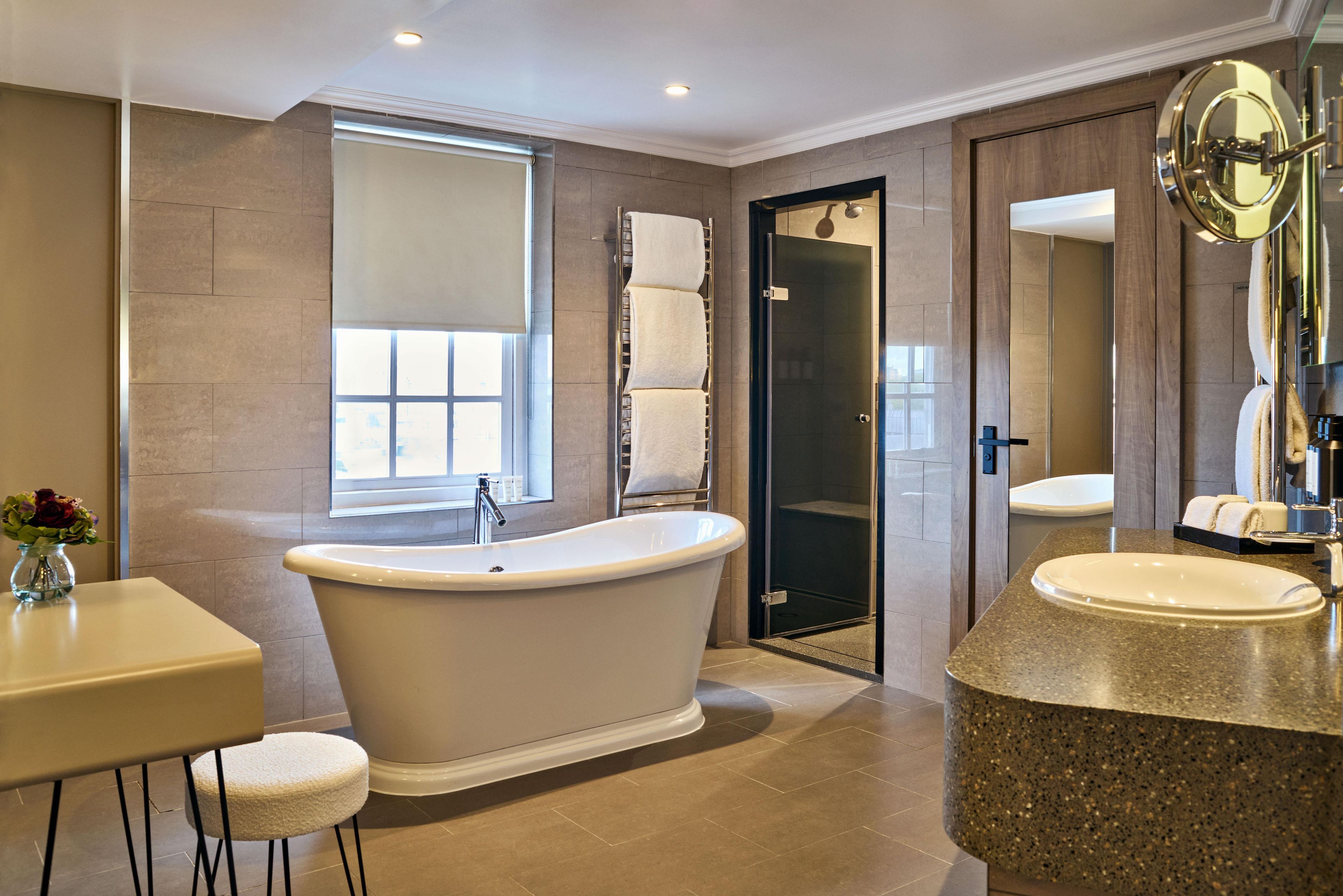 A modern bathroom with a freestanding bathtub, a vanity with a granite countertop, and a large mirror.