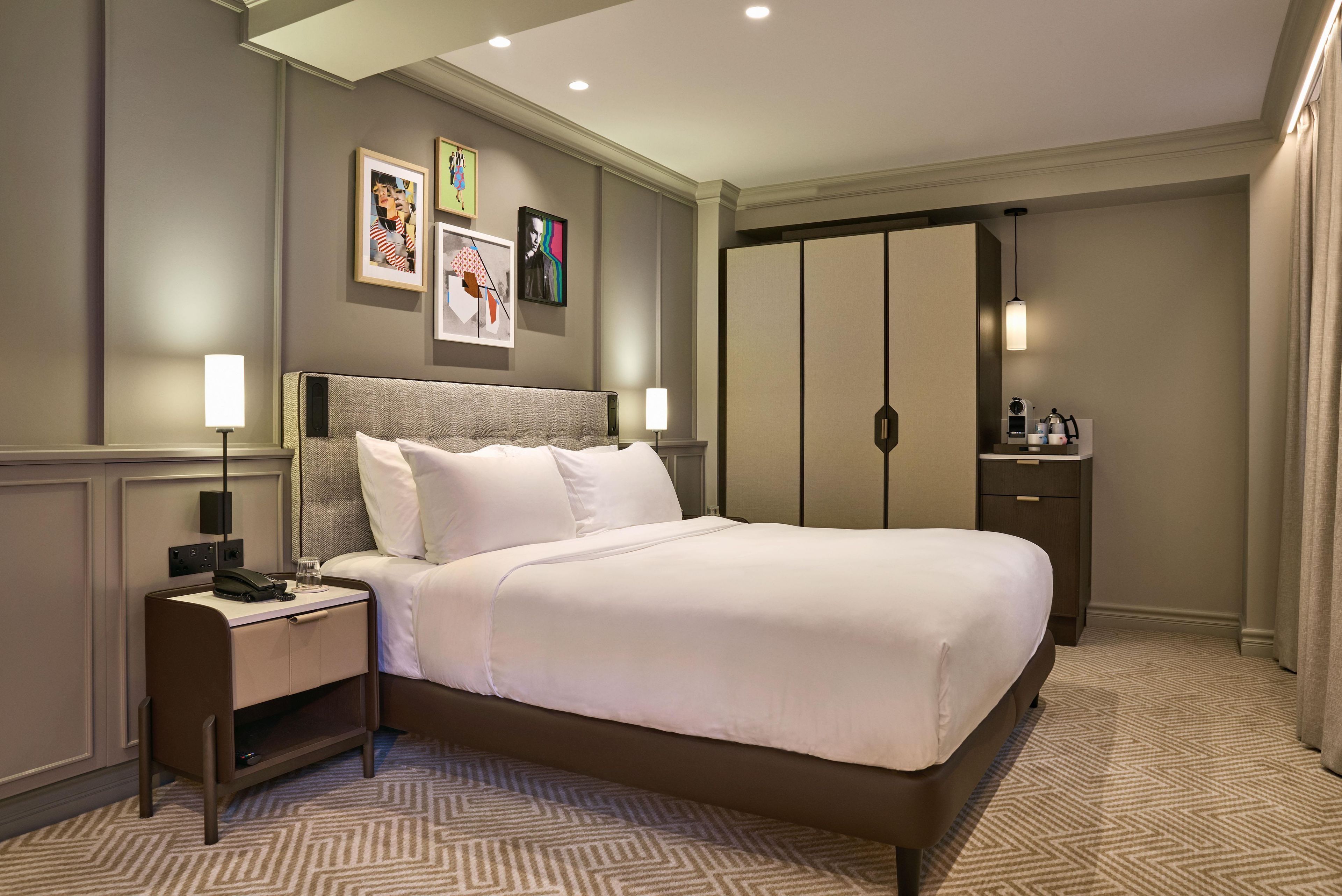 Ein Hotelzimmer mit einem großen Bett, Nachttischen mit Lampen, einem Kleiderschrank und Bildern an den Wänden.