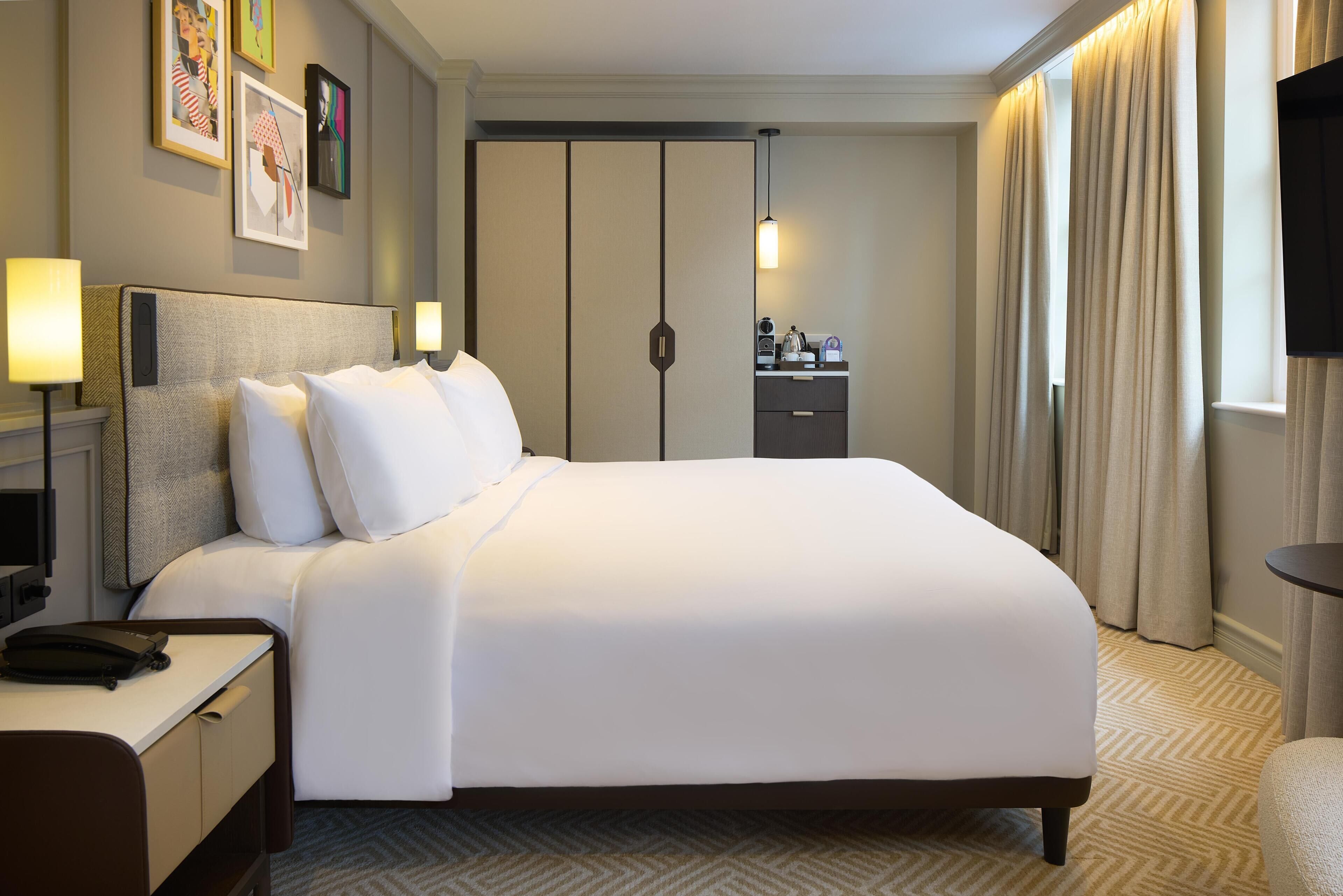 A hotel room with a bed, bedside table, lamp, desk, and a wardrobe.