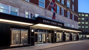Entrada del Hotel Bond Street, con fachada moderna, puertas de vidrio grandes y una bandera.