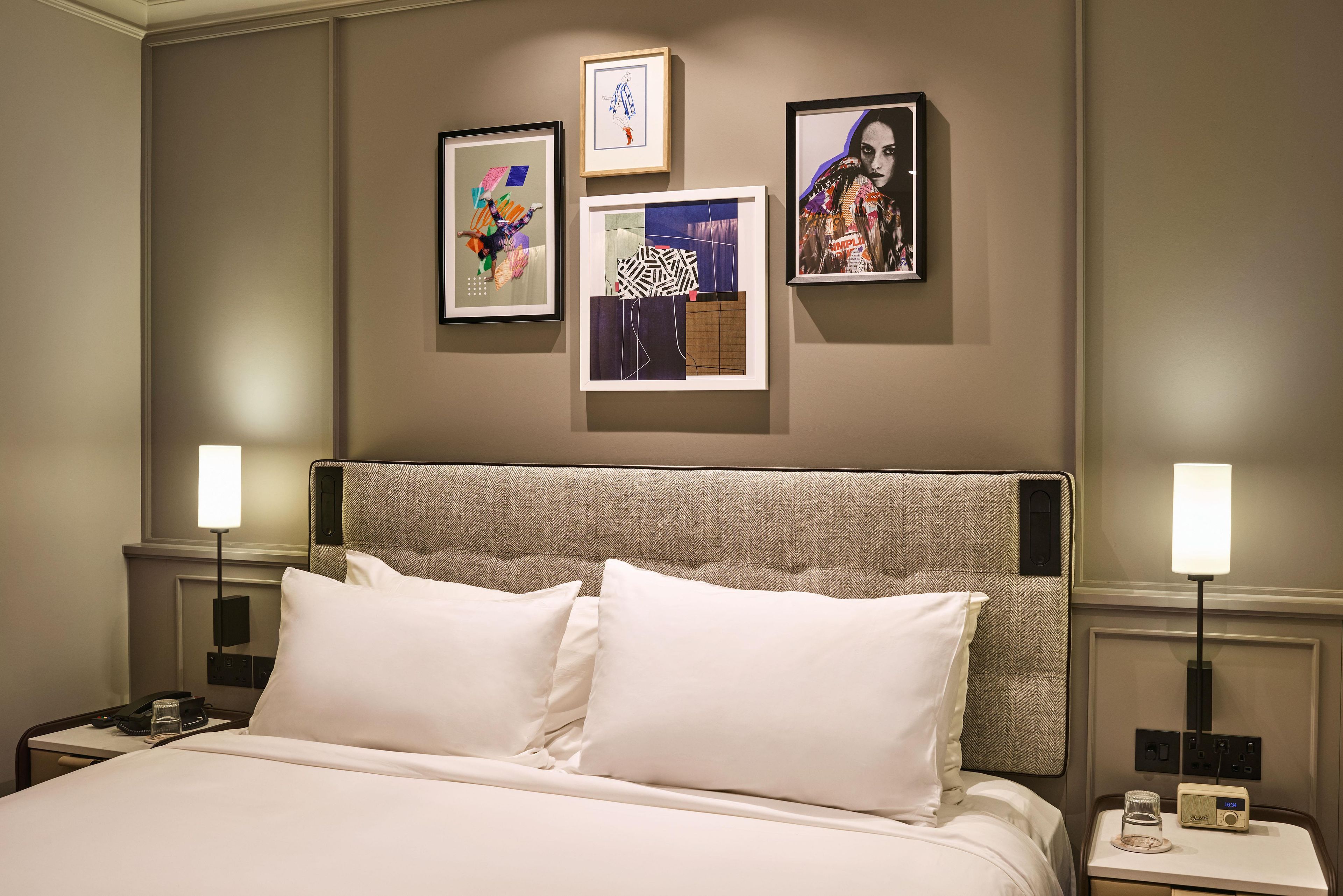 A hotel room with a large bed, two bedside tables, a headboard, and three framed artworks on the wall.