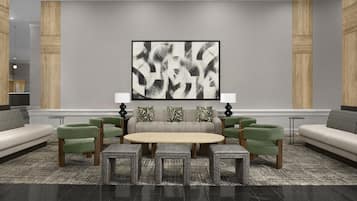 A modern lounge area with a central round table, green upholstered chairs, a grey sofa, and a large abstract painting on the wall.