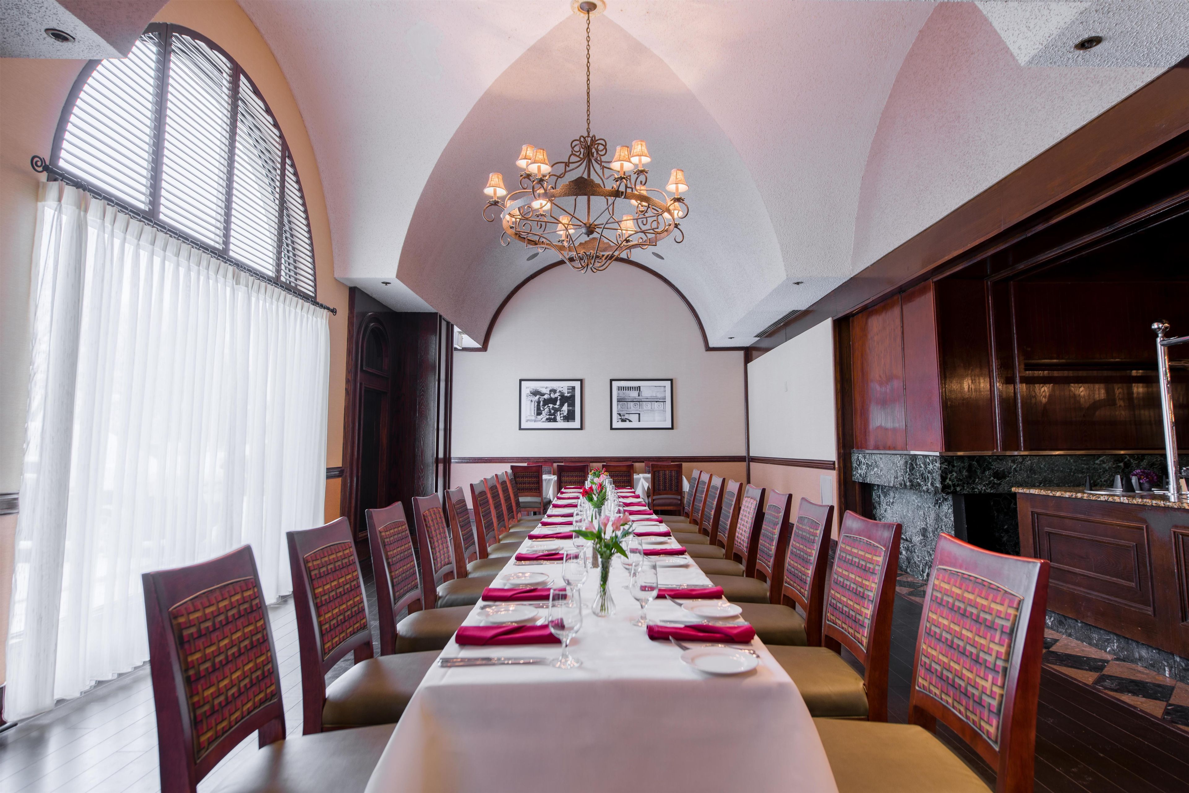 A long dining table set with chairs, a chandelier, and framed pictures on the wall.