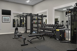 Un gimnasio con equipo de levantamiento de pesas, mancuernas y máquinas de ejercicio.