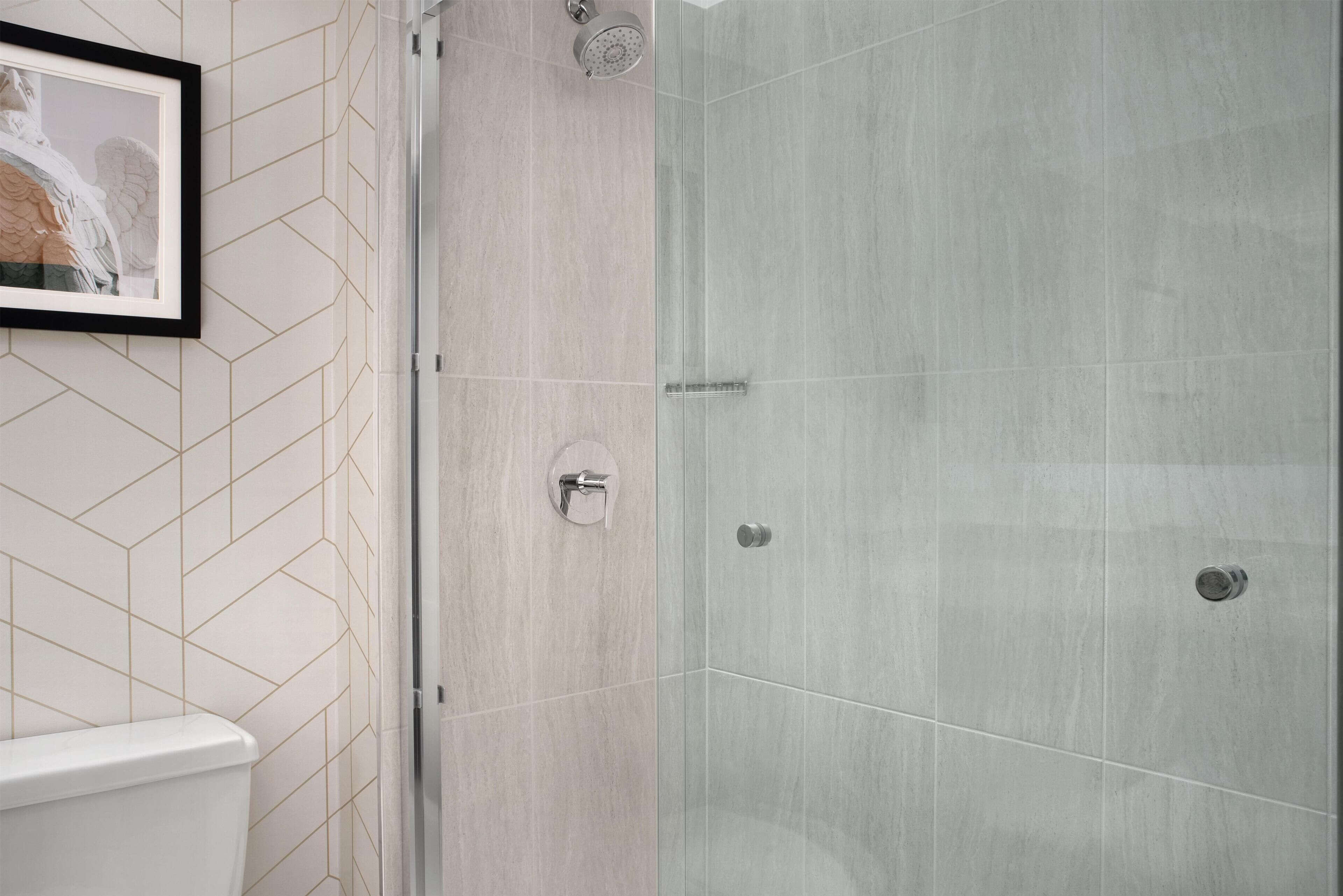 A bathroom with a toilet, a shower with a glass door, and a framed picture on the wall.