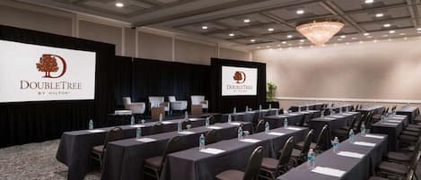 Un salón de conferencias con varias mesas, sillas y una pantalla grande mostrando el logotipo de DoubleTree by Hilton.