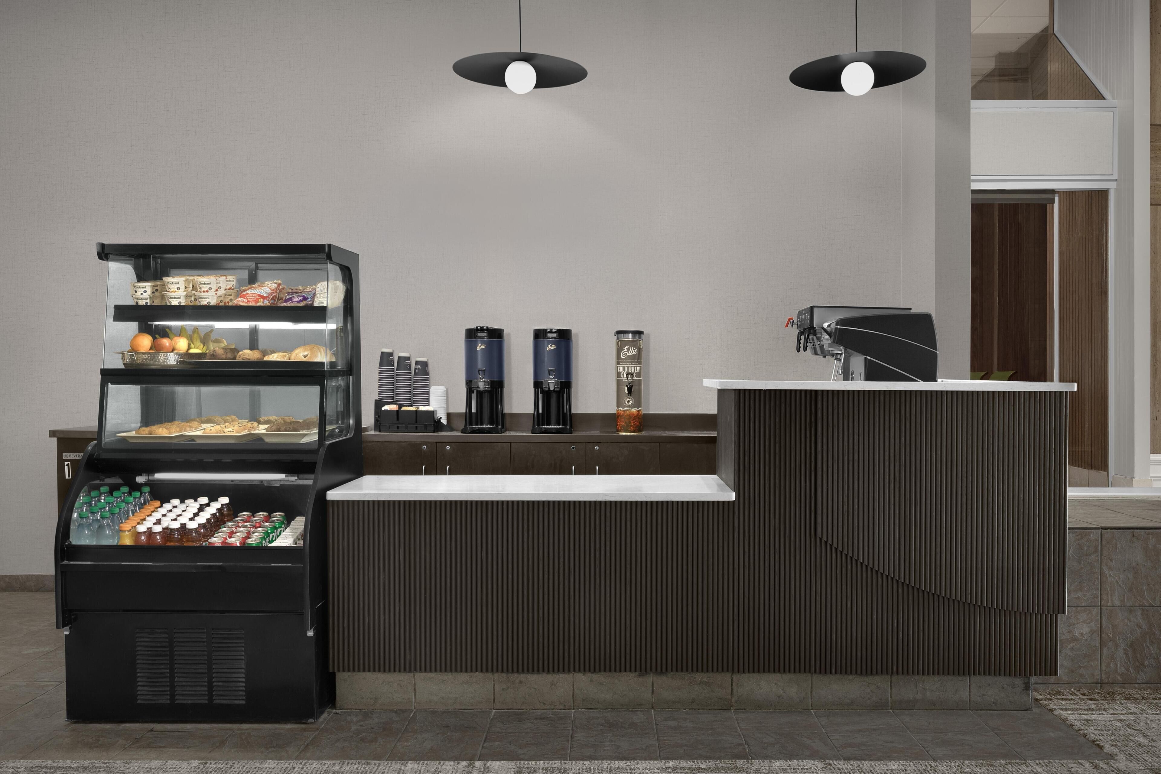 Un espace de libre-service proposant des boissons, avec un présentoir réfrigéré, des machines à café et un comptoir équipé d’une machine à café.