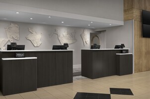 Un espace d’accueil d’hôtel comprenant deux comptoirs de réception, un design moderne et un téléviseur à écran plat fixé au mur.