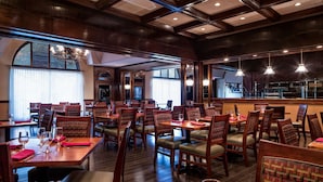 A restaurant with wooden tables and chairs, large windows, and hanging lights. - Doubletree by Hilton Philadelphia Airport (Philadelphia)