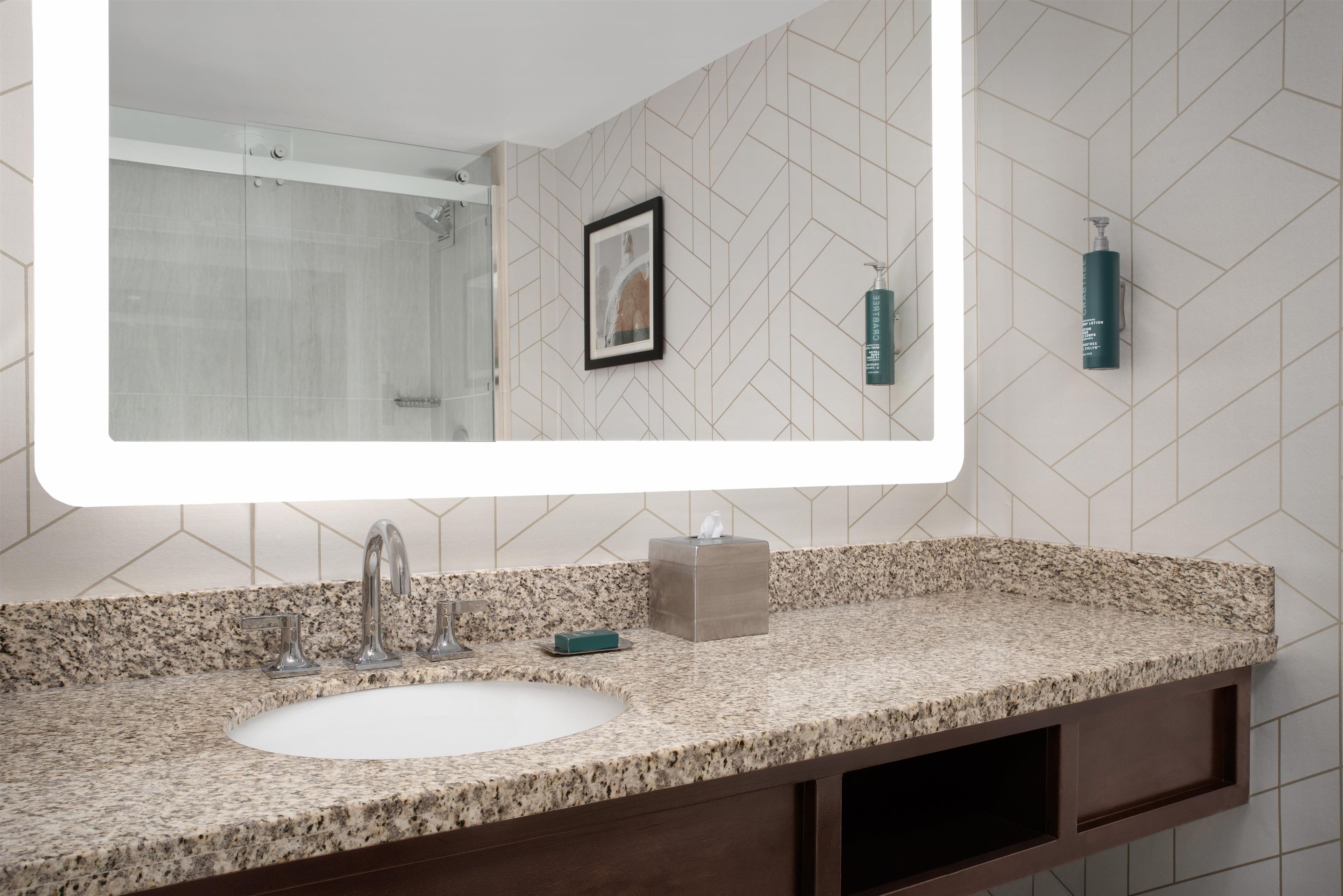 A bathroom with a large mirror, a sink, a shower, and a towel dispenser.