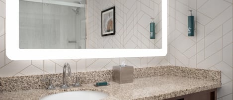 A bathroom with a large mirror, a sink, a shower, and a towel dispenser.