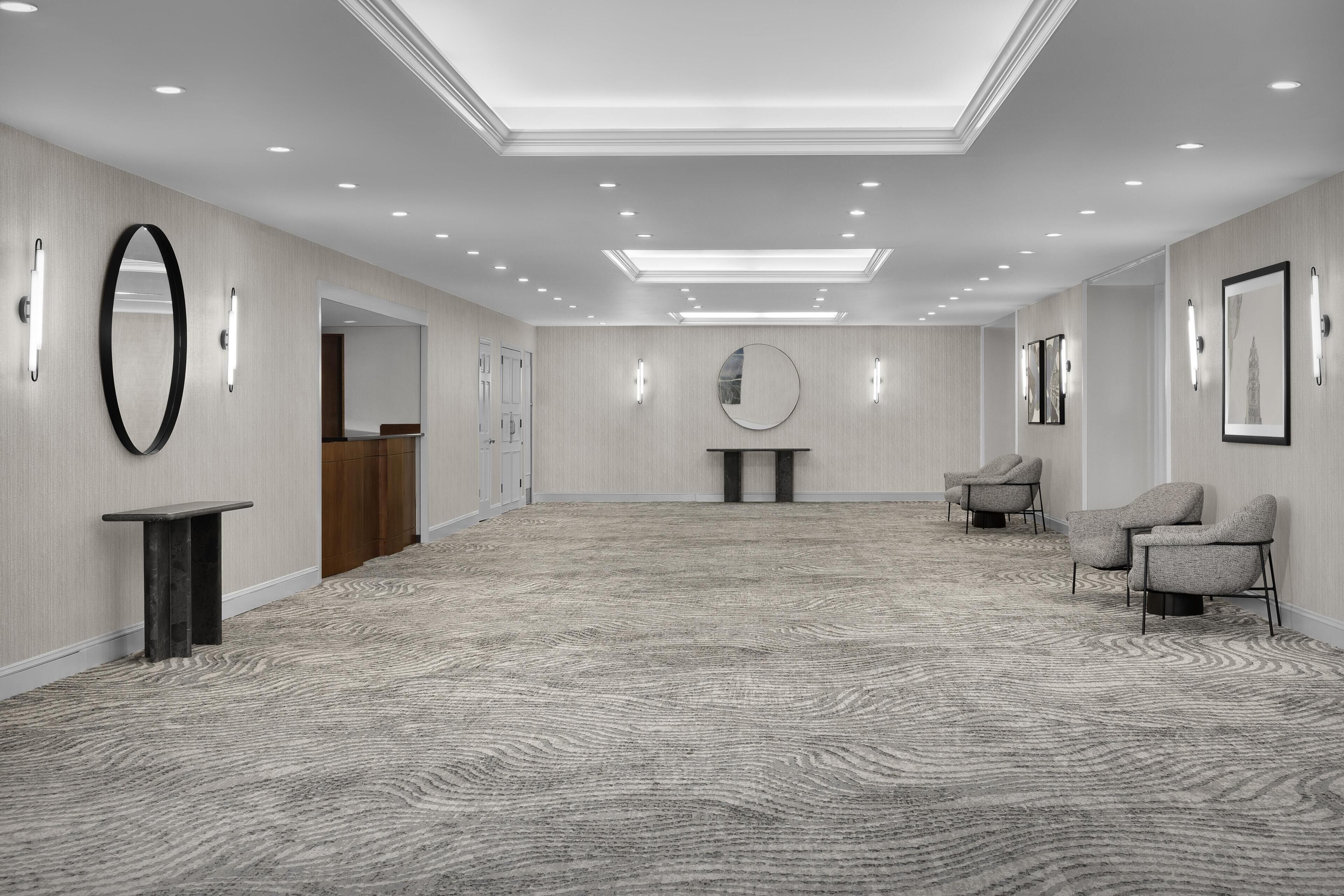En rymlig hotellobby med högt i tak, infälld belysning, en receptionsdisk, en rund spegel och en sittgrupp.