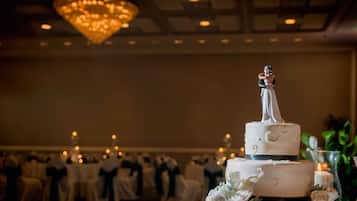 A wedding cake with a topper, surrounded by tables with chairs, and a chandelier in the background.