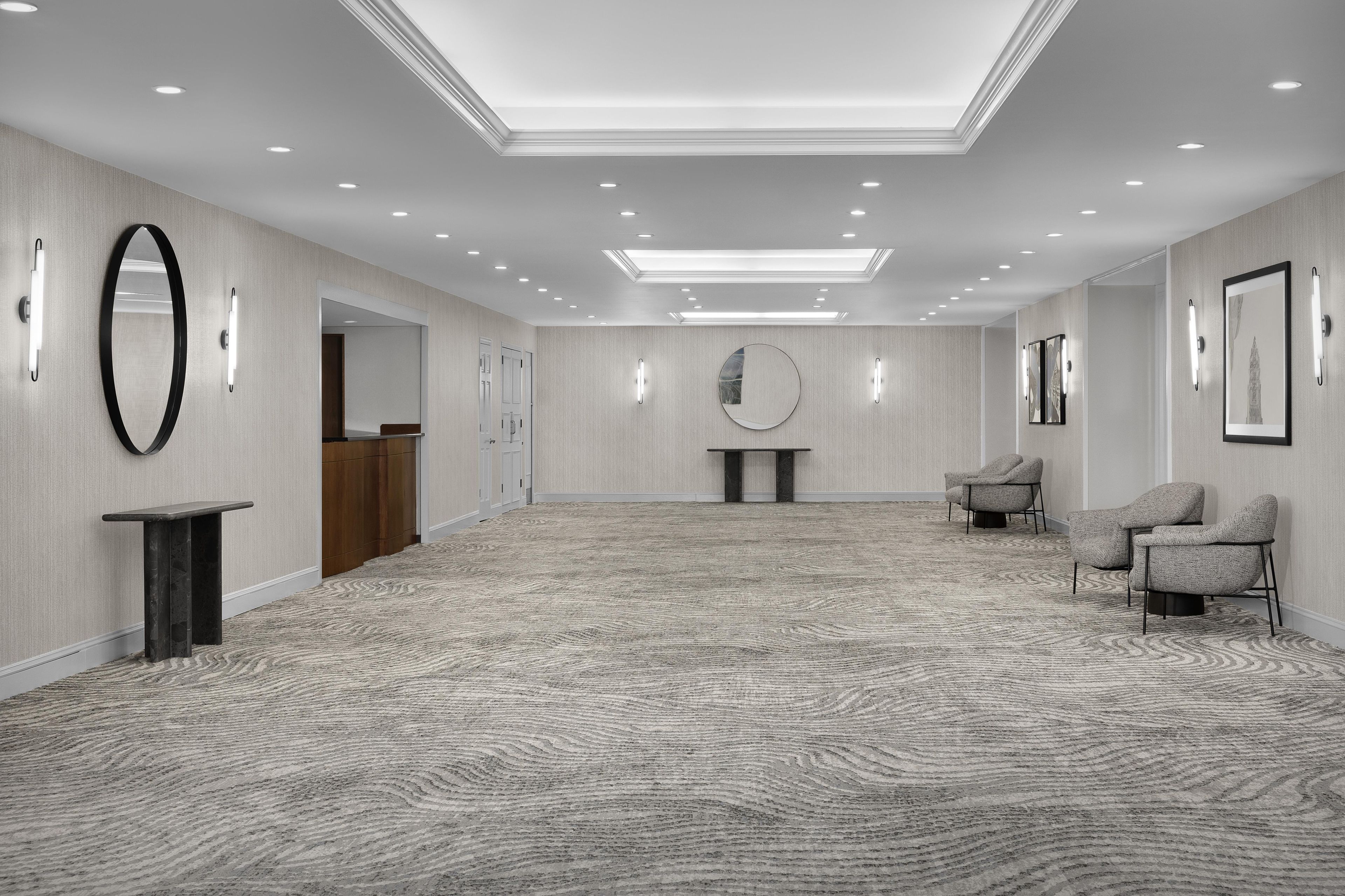 A spacious hotel lobby with a high ceiling, recessed lighting, a reception desk, a round mirror, and seating area.