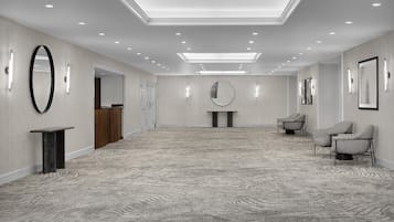 A spacious hotel lobby with a high ceiling, recessed lighting, a reception desk, a round mirror, and seating area.
