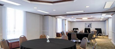 A conference room with a round table, chairs, a chandelier, and a framed picture on the wall.