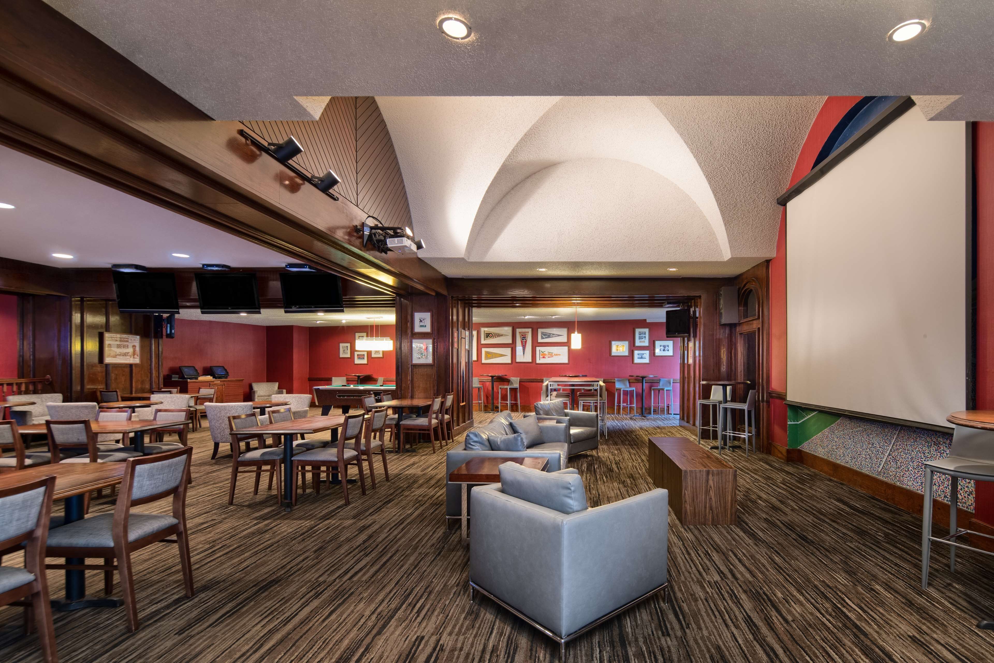 A hotel lobby with multiple seating areas, including sofas and tables, and a large screen for presentations.