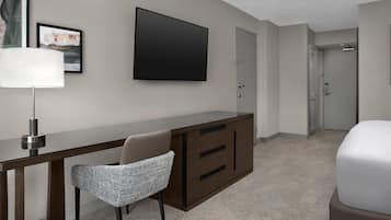 Habitación de hotel con escritorio, silla, televisión y armario.