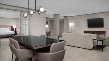 A hotel room with a dining table, chairs, a sofa, a TV, and a bed.