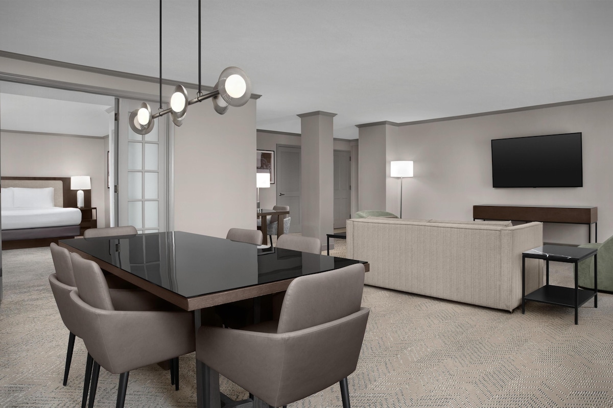 Una habitación de hotel con una mesa de comedor, sillas, un sofá, un televisor y una cama.