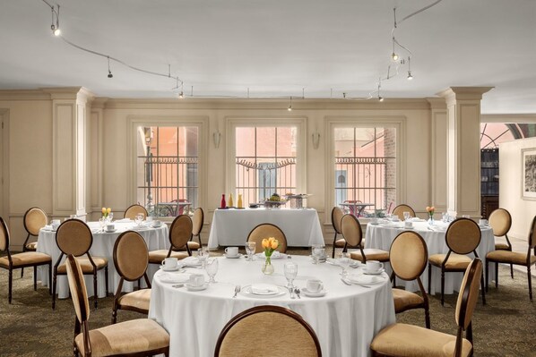 A formal dining room with round tables, chairs, and a central buffet table.